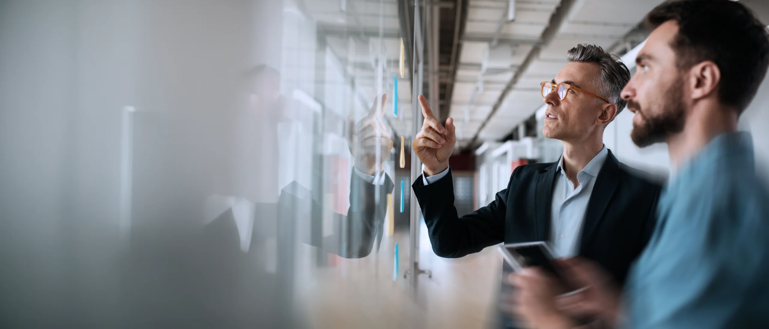 Business people meeting planning start up, talking, discussing ideas, brainstorming. Scrum master using sticky notes standing near planning board in modern office